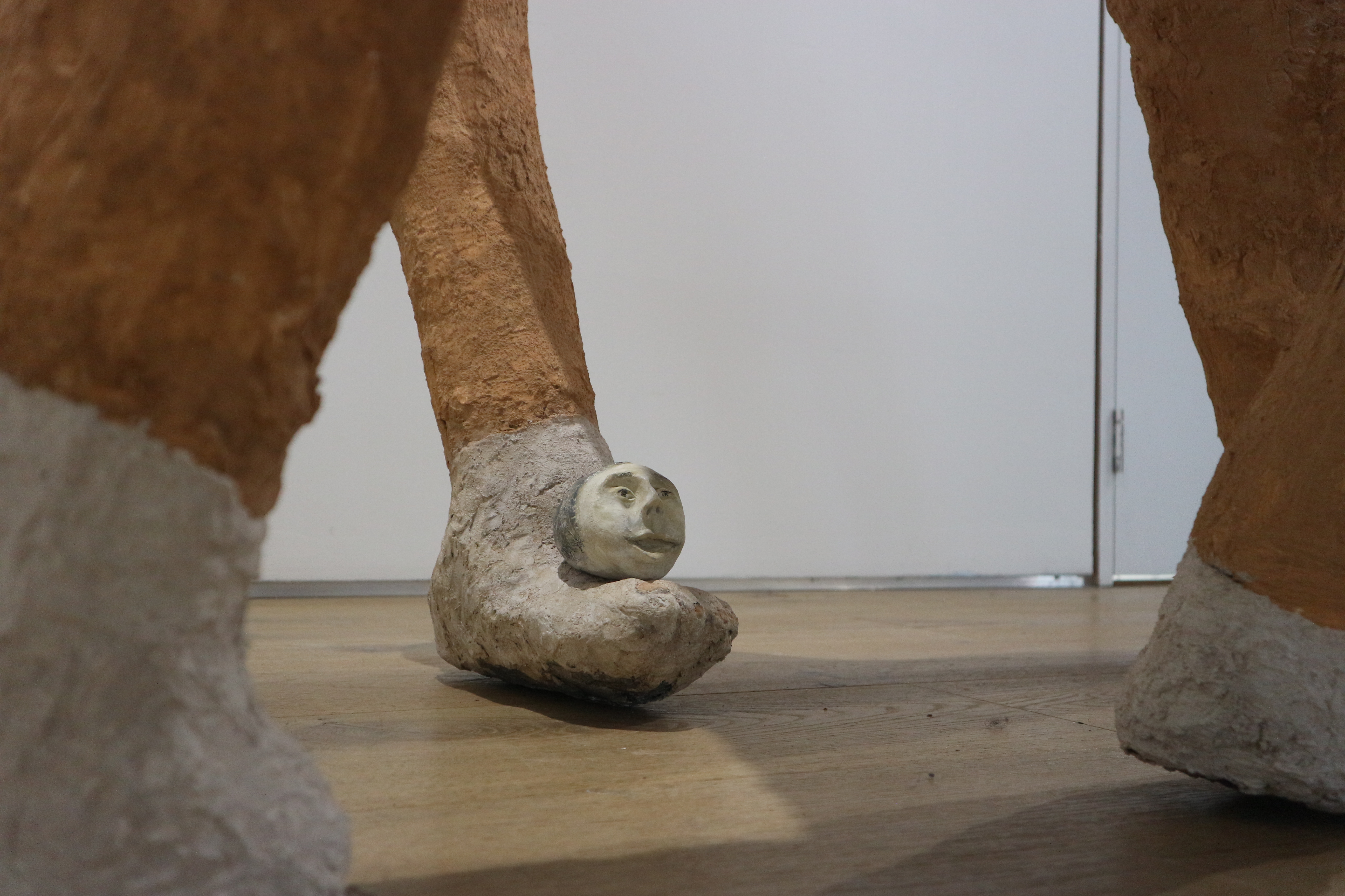 Close up photo of the feet of an abstract sculpture of humanoid figure. The foot in focus has a small round head resting on top of it.