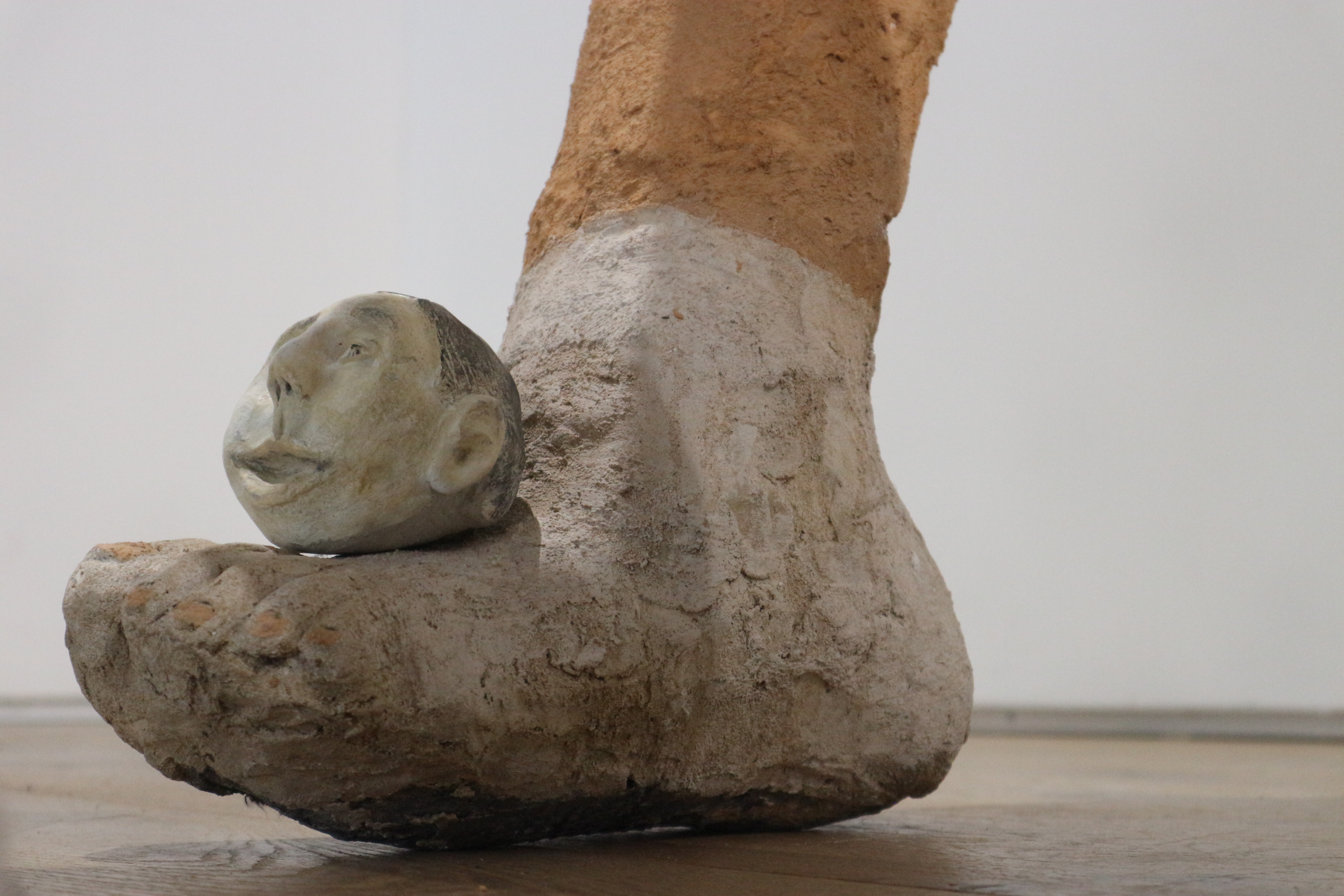Close up photo of the feet of an abstract sculpture of humanoid figure. The foot in focus has a small round head resting on top of it.