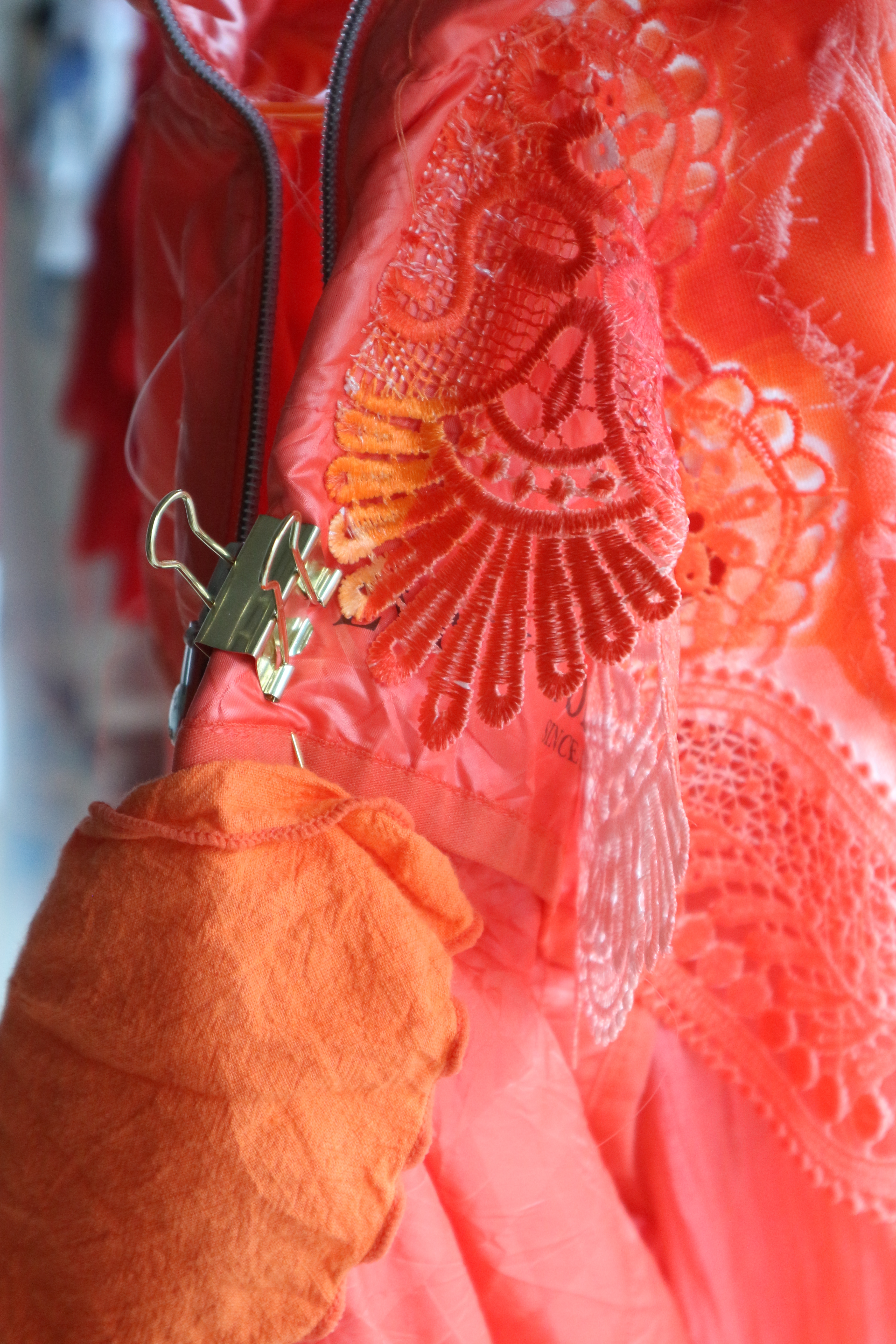 Close up photo of bright red and orange fabric of different textures, held by a gold bulldog clip.