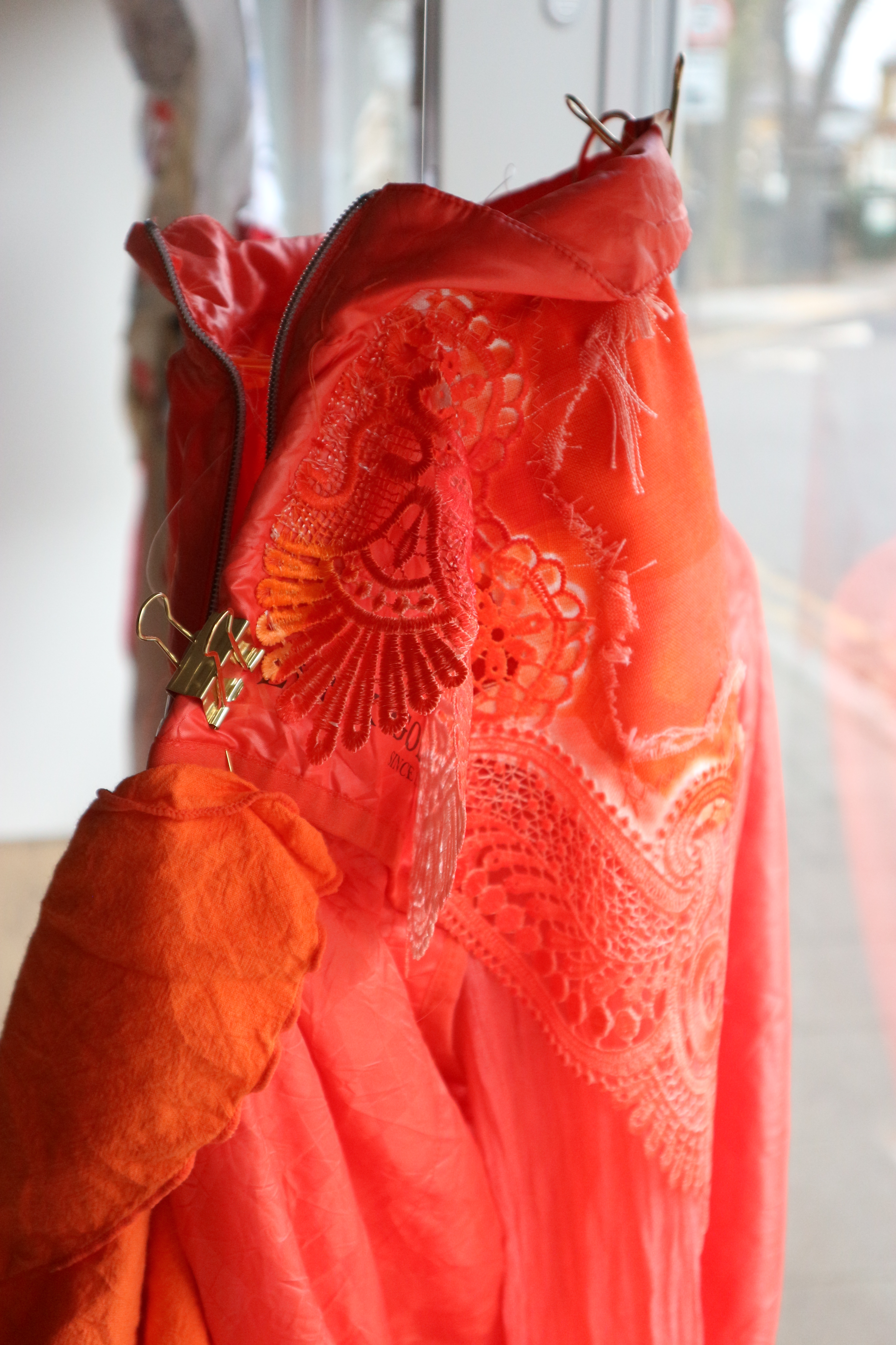 Close up photo of bright red and orange fabric of different textures, held by a gold bulldog clip.