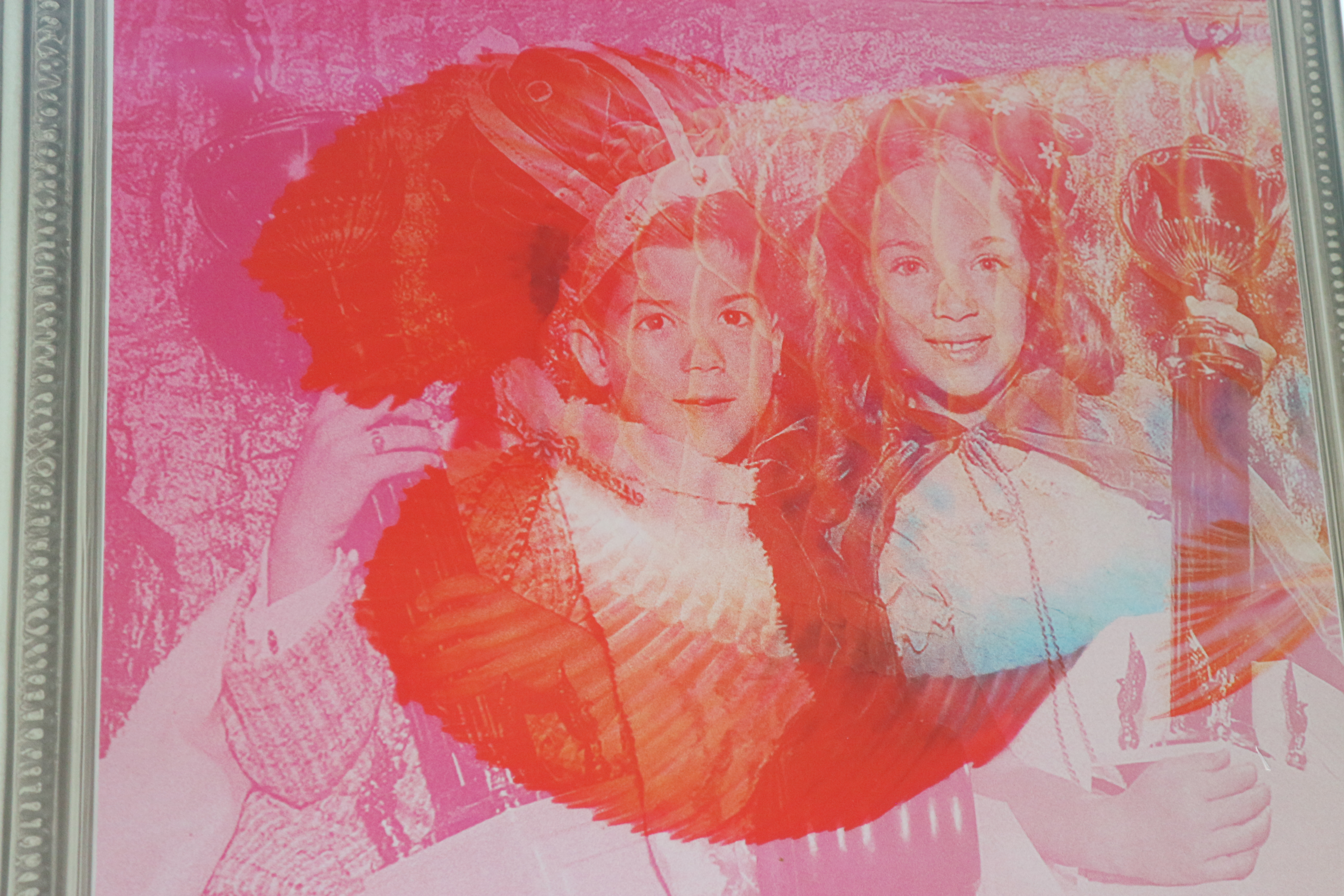 Close up photo of a digital pint in orange, white and pink with a silver frame. It shows two young children holding a trophy and fish scales.