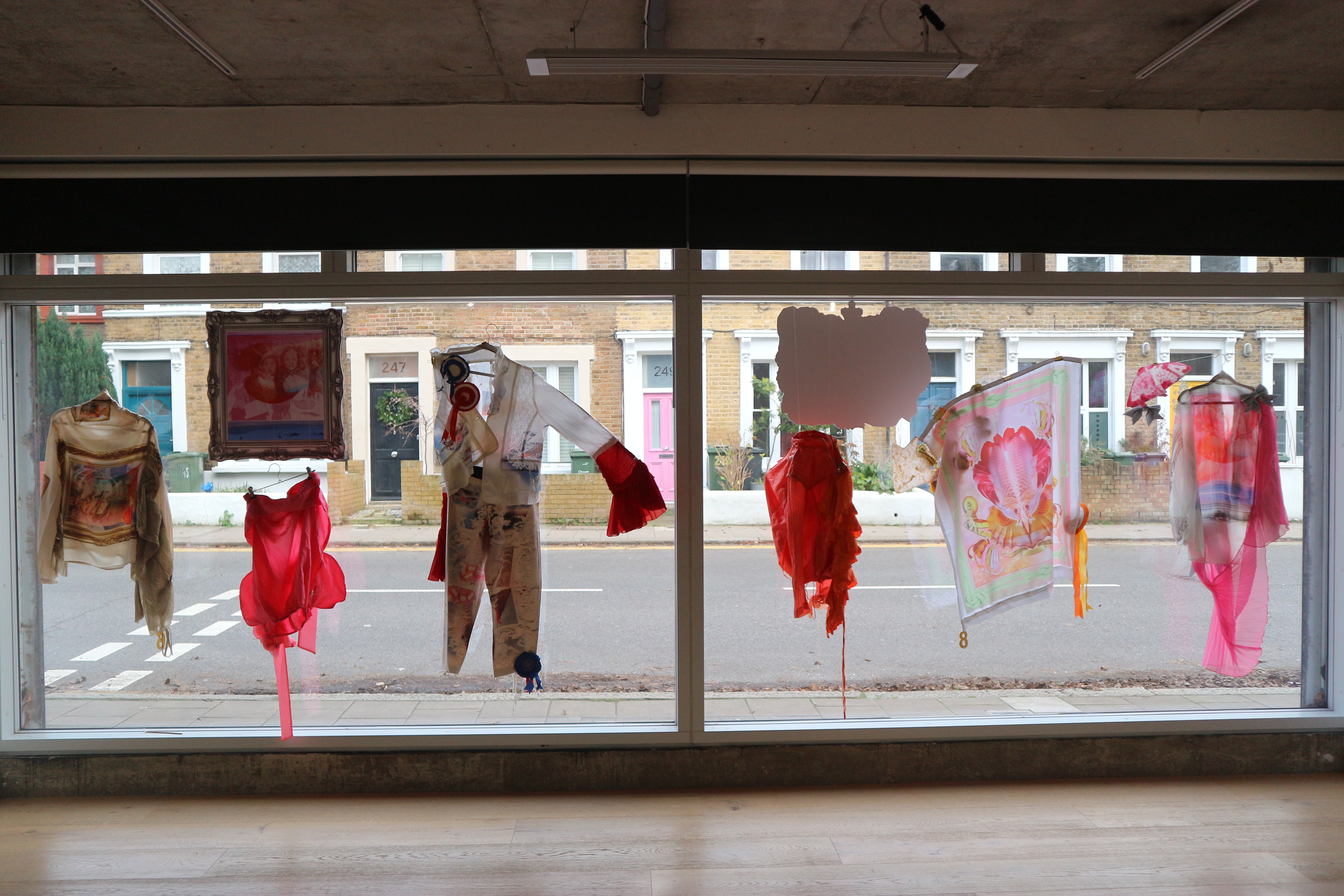 Photograph of a long gallery window with various textile artworks hung in the window as a display.