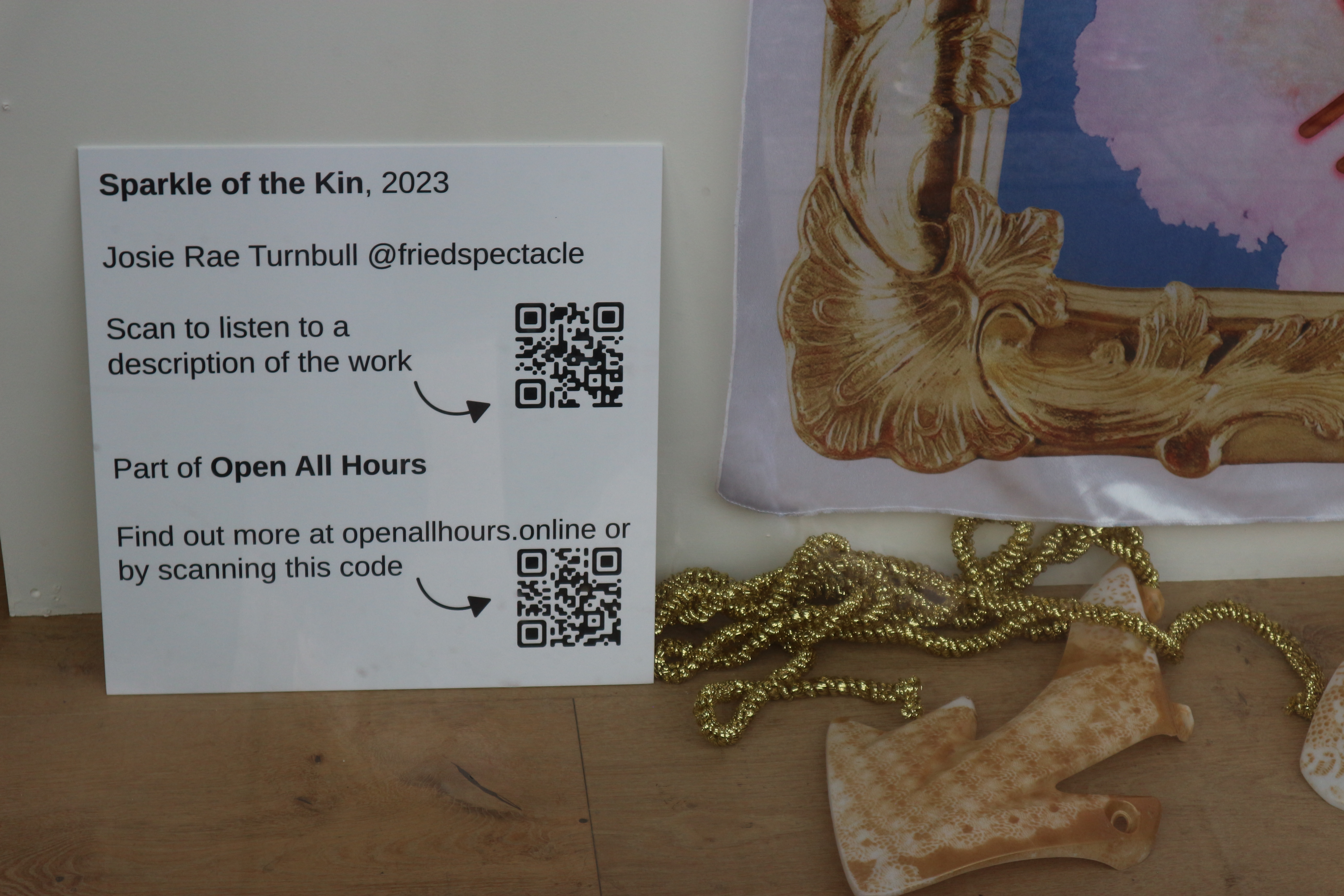 Close up of the artwork captions for a textile work which includes QR codes. All information is available on the exhibition website.