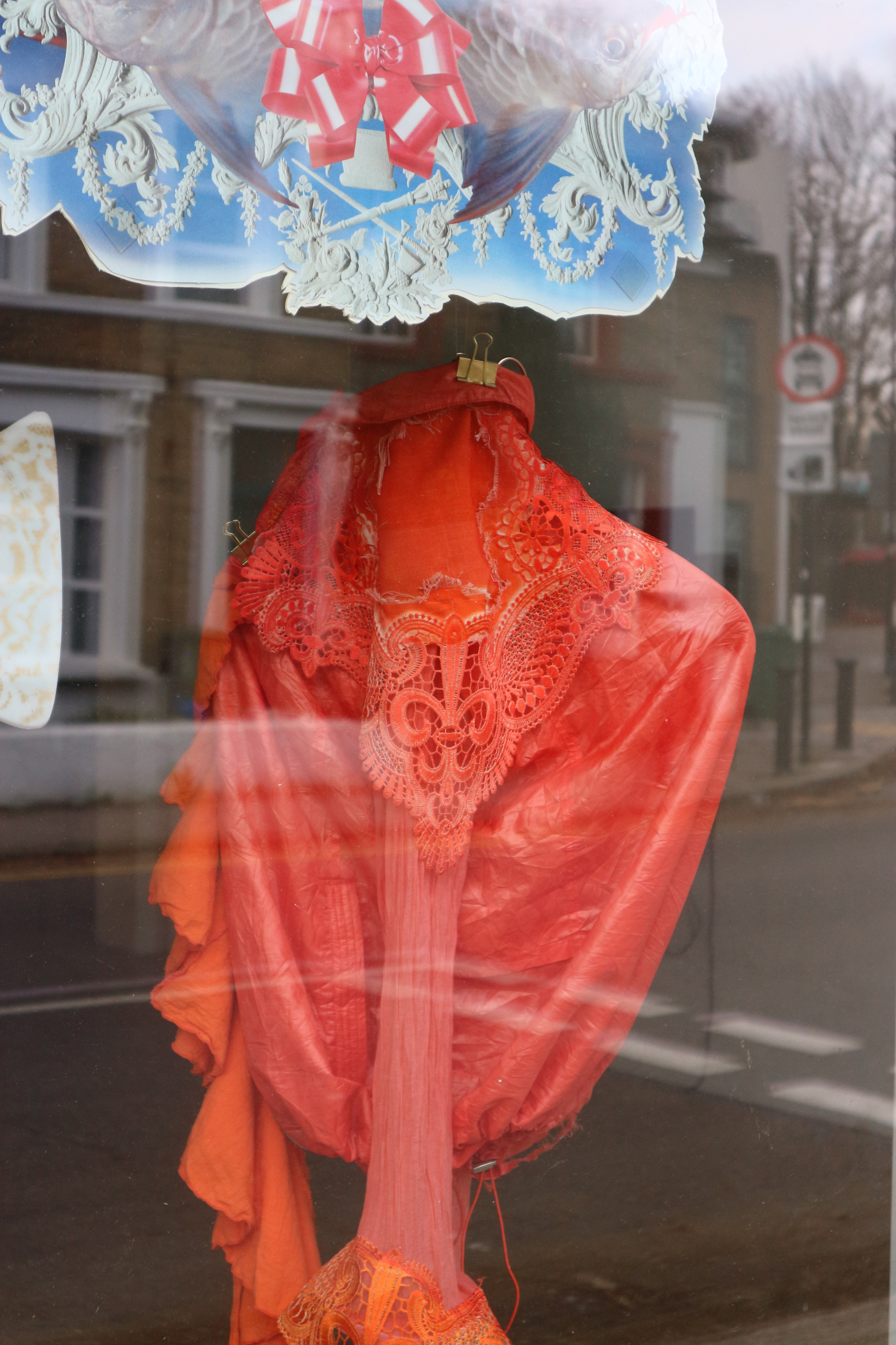 Close up photo of bright red and orange fabric of different textures, held by a gold bulldog clip.