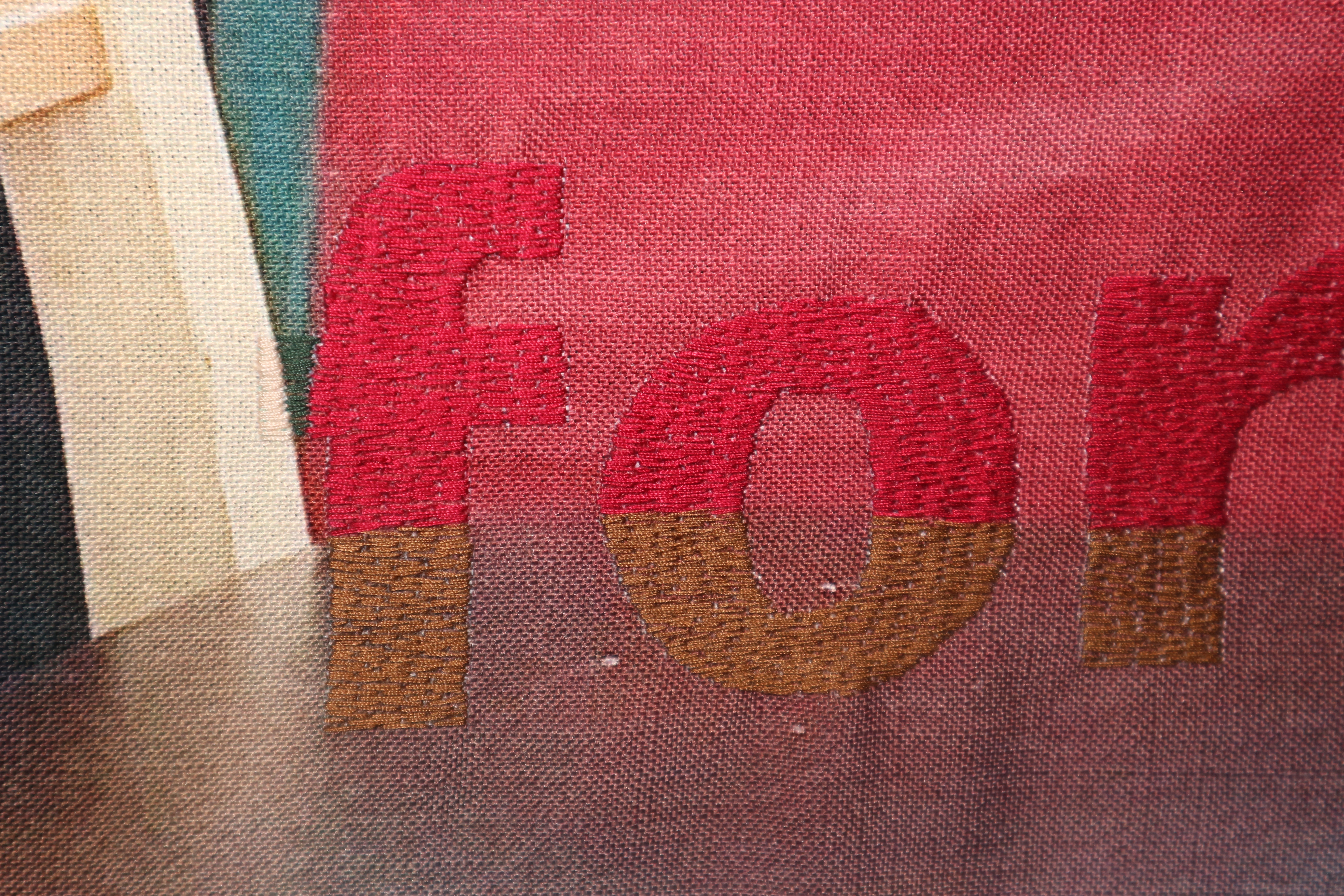 Close up photo of a textile artwork. The word 'for' is stitched in thick letters in red and brown to match the textile background behind.