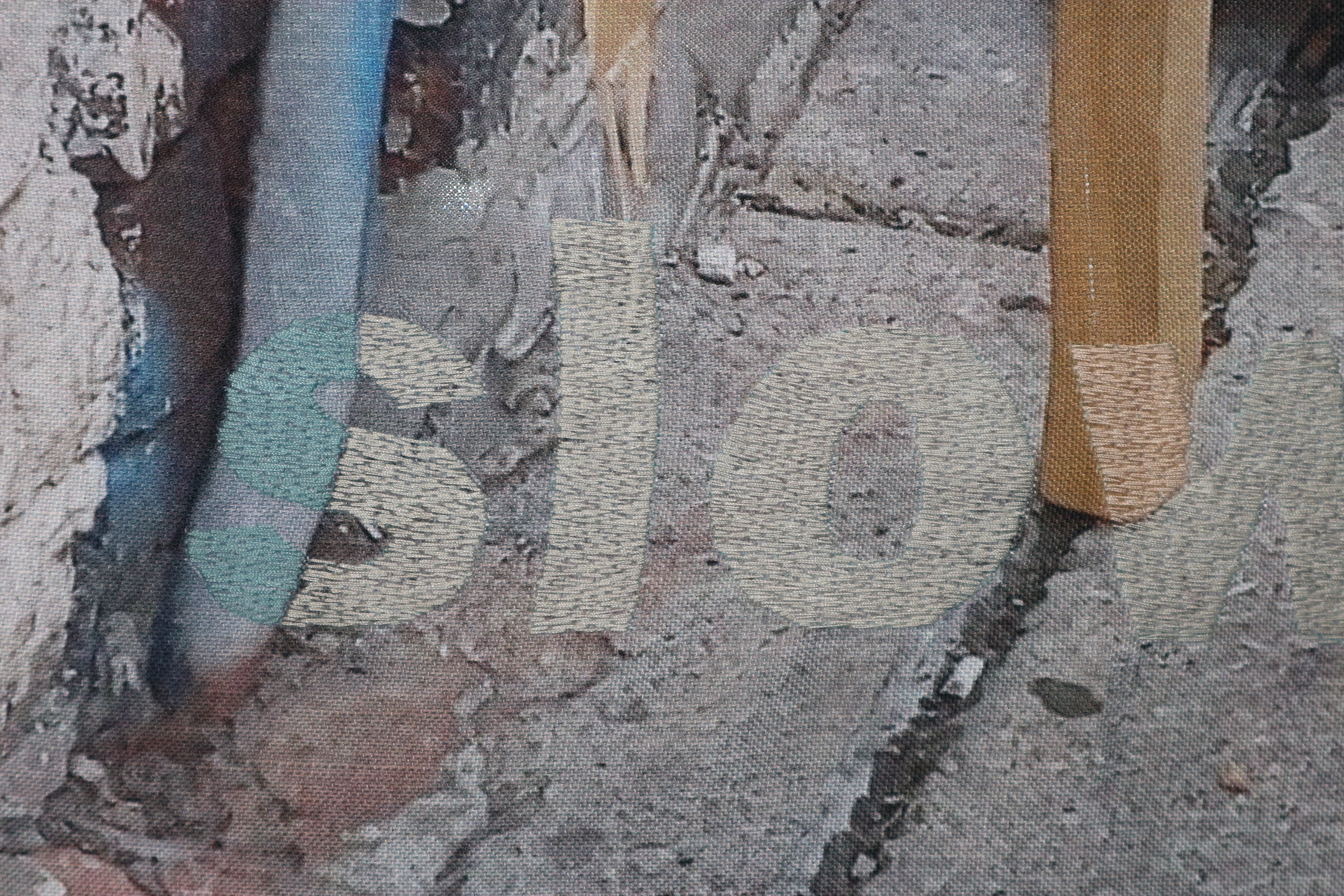 Close up photo of a textile artwork. The word 'slow' is stitched in thick letters in grey and beige to match the textile background behind.