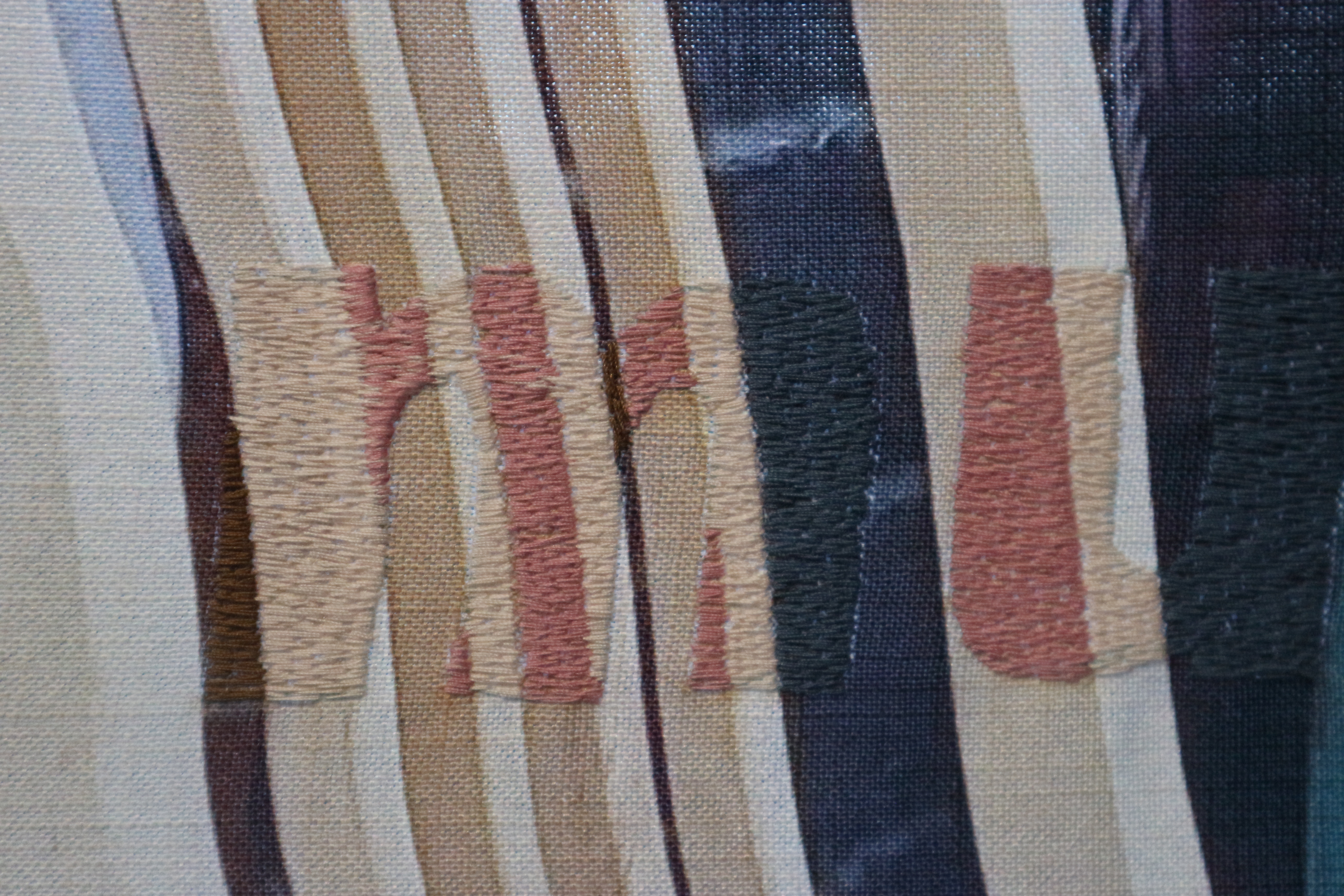 Close up photo of a textile artwork. The letters 'mu' are stitched in thick letters in brown and beige to match the textile background behind.